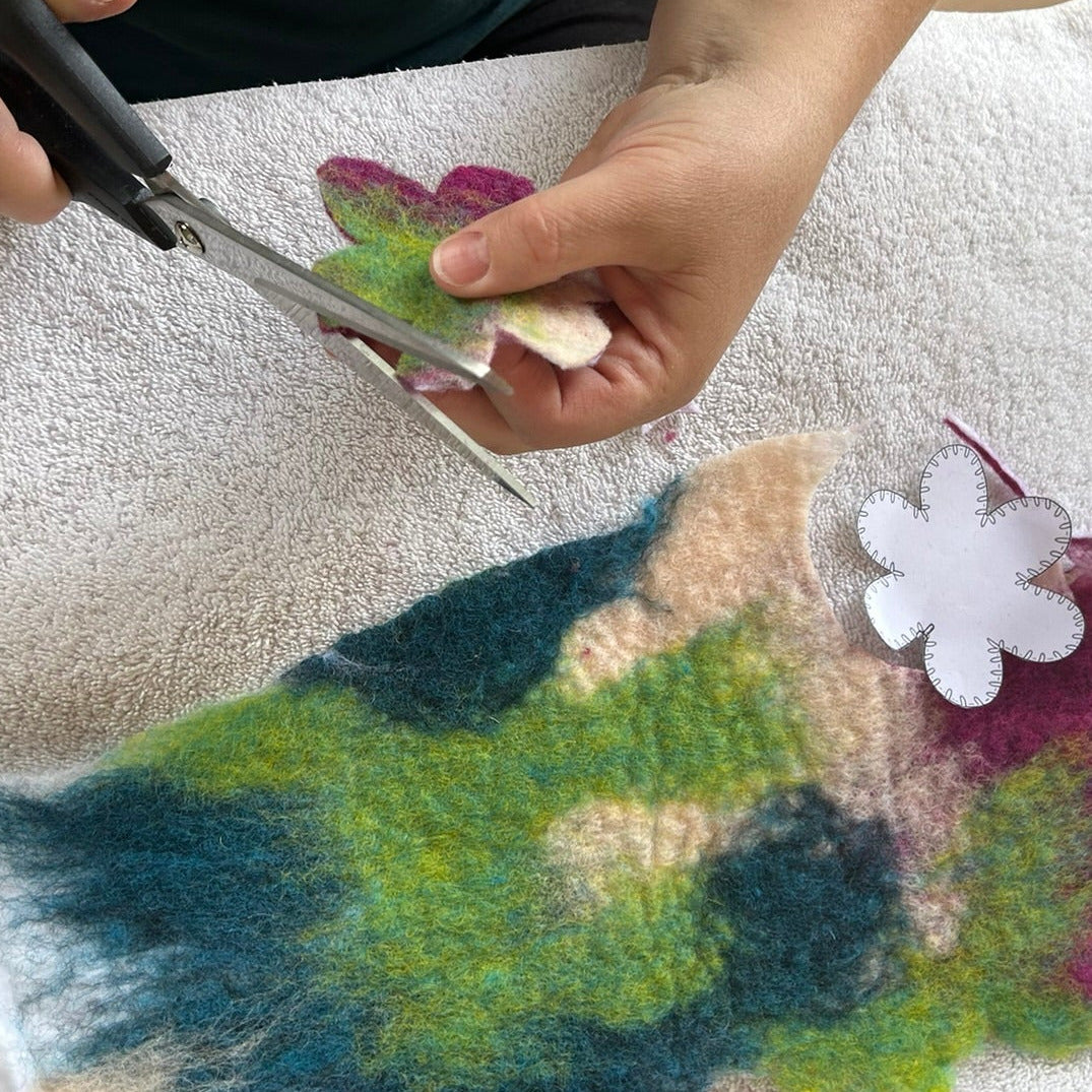 A person's hands with scissors, cutting out wool felt with a template.