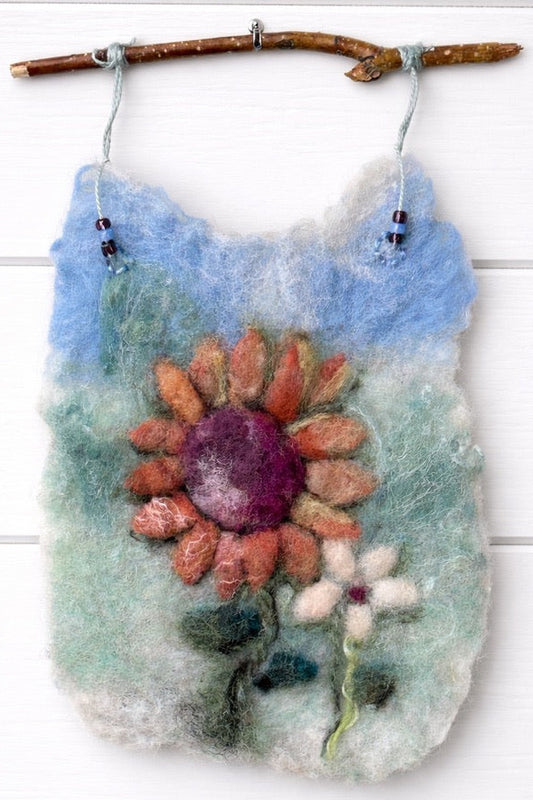 Felted wall hanging with a floral design on a white wooden background