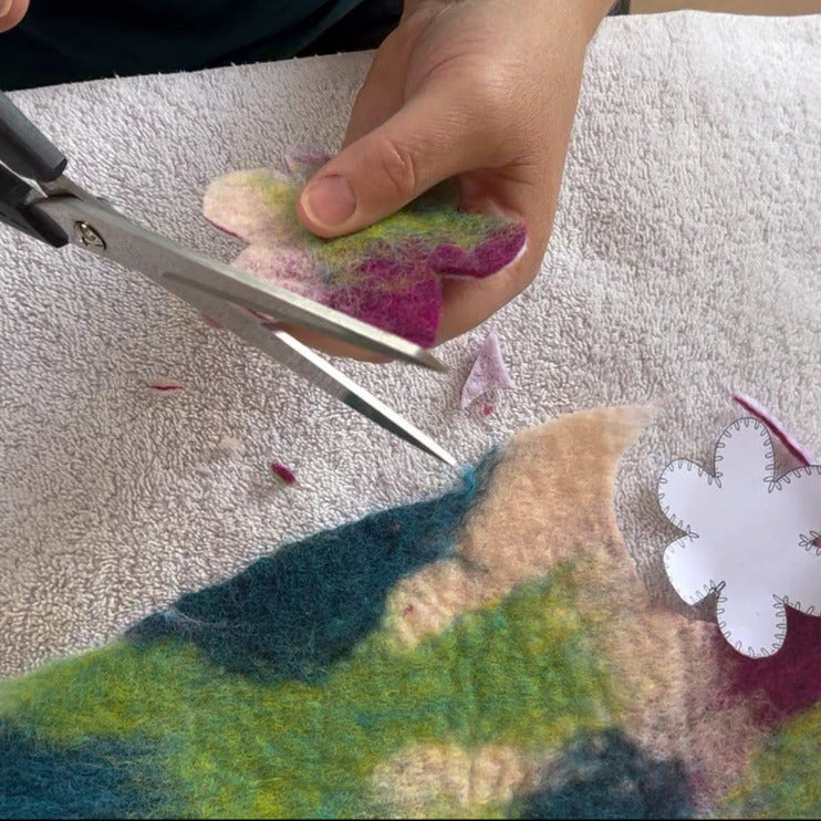 A person's hands cutting out a heart on felt with a paper template.