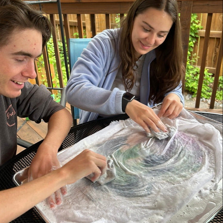 Two people wet felting using a soap and water on top of fabric and wool.